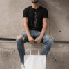 t shirt mockup of a bearded man with a tote bag sitting on a concrete structure 29412 - Varegue